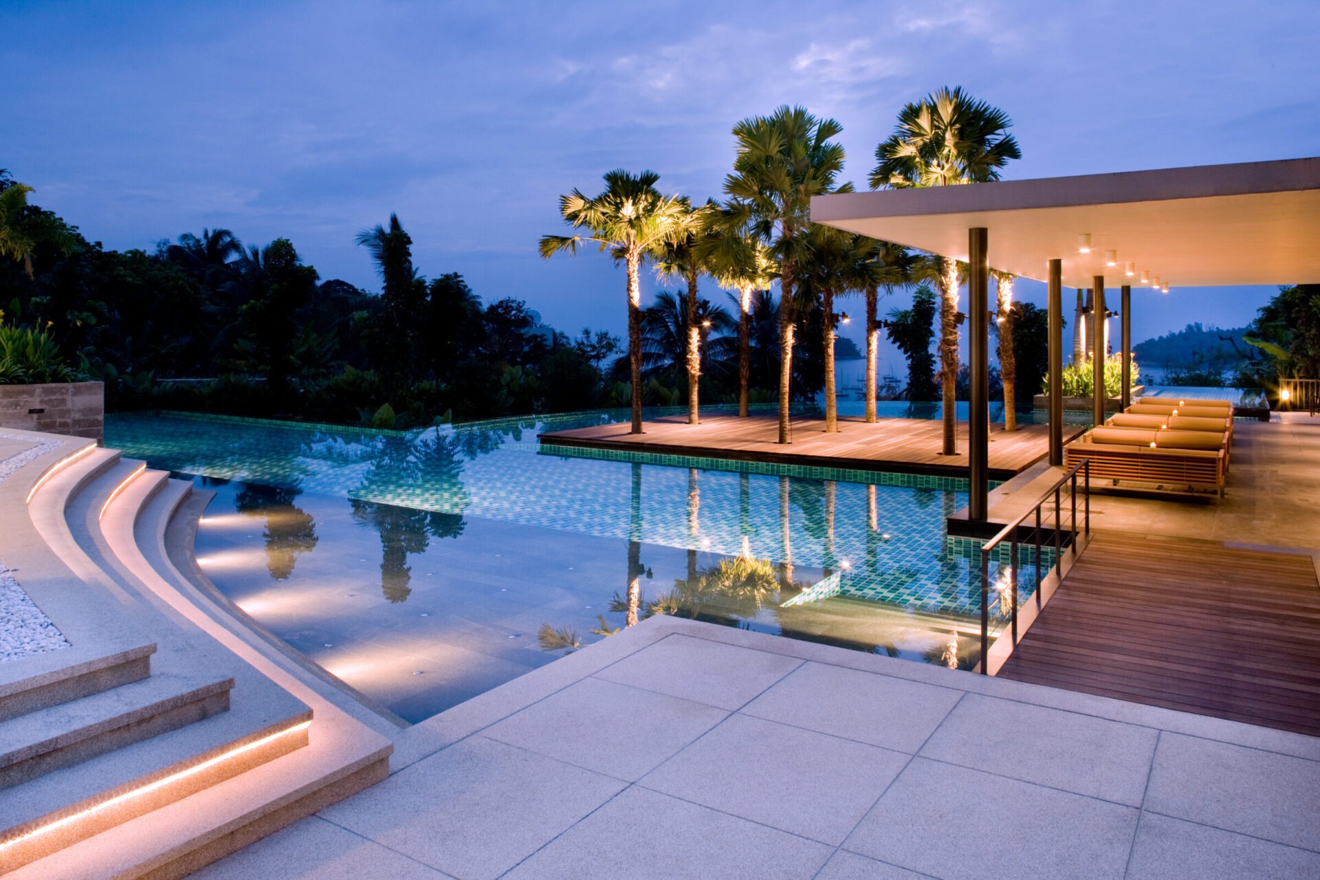 Night view of an infinity pool with illuminated palm trees.