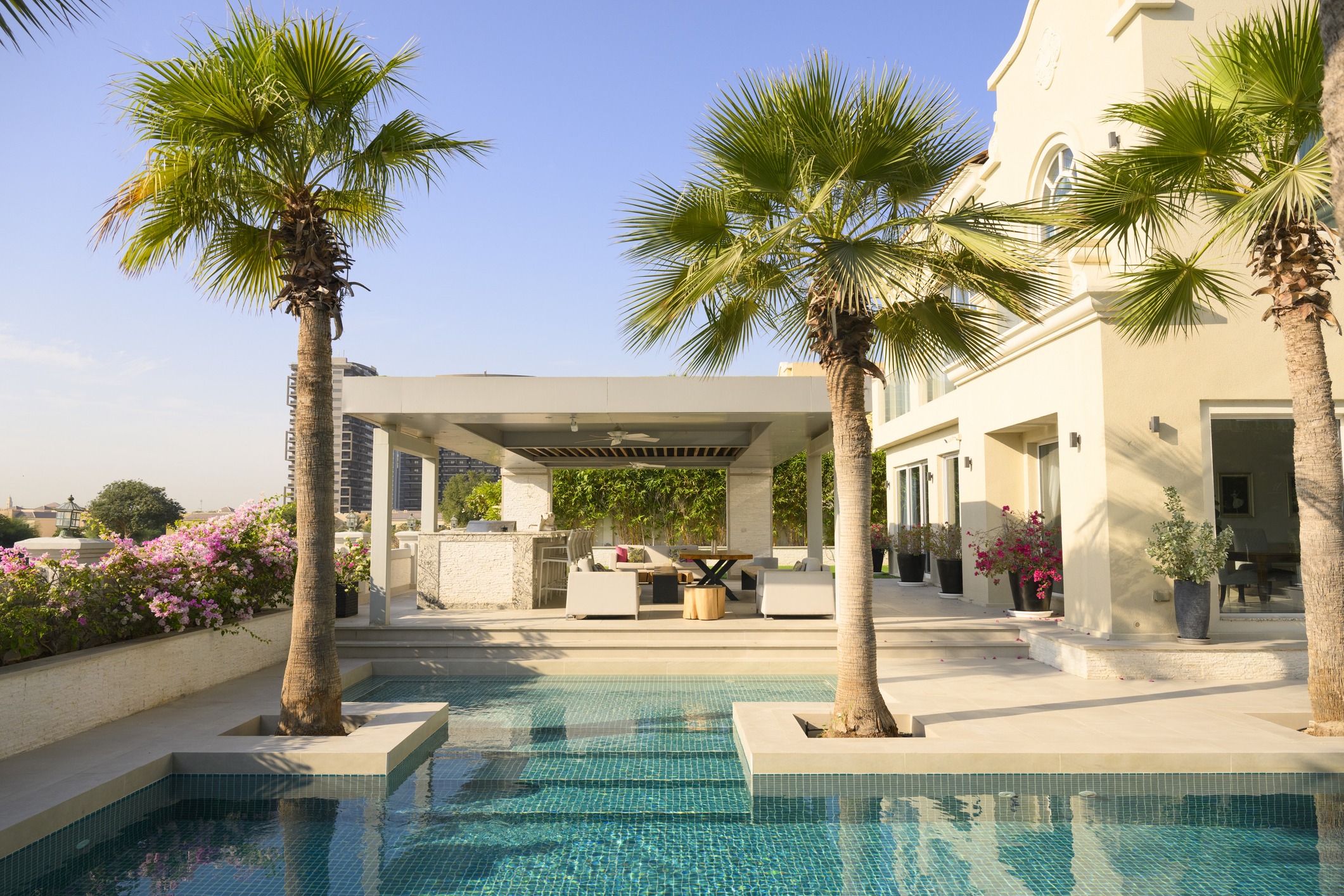 A luxurious villa patio with a pool, palm trees, and outdoor seating.