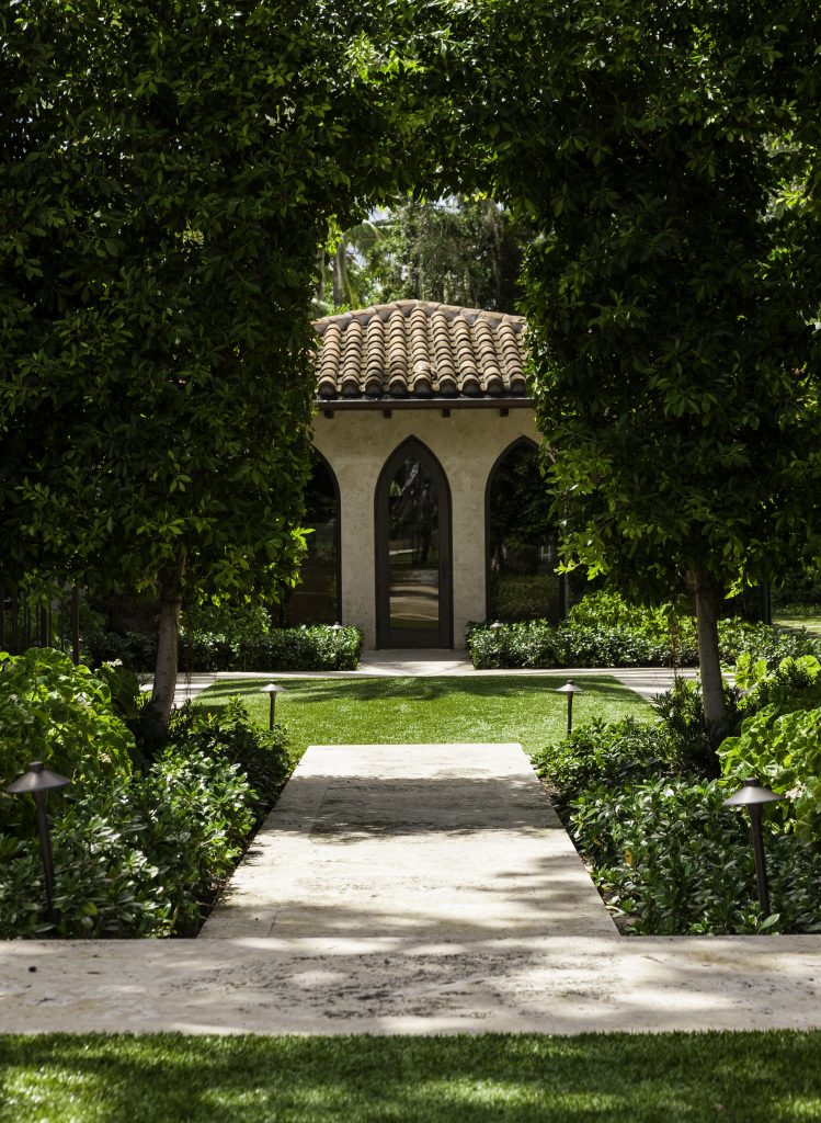 A scenic garden path leads to a quaint building with arched windows and a tiled roof, surrounded by lush greenery.
