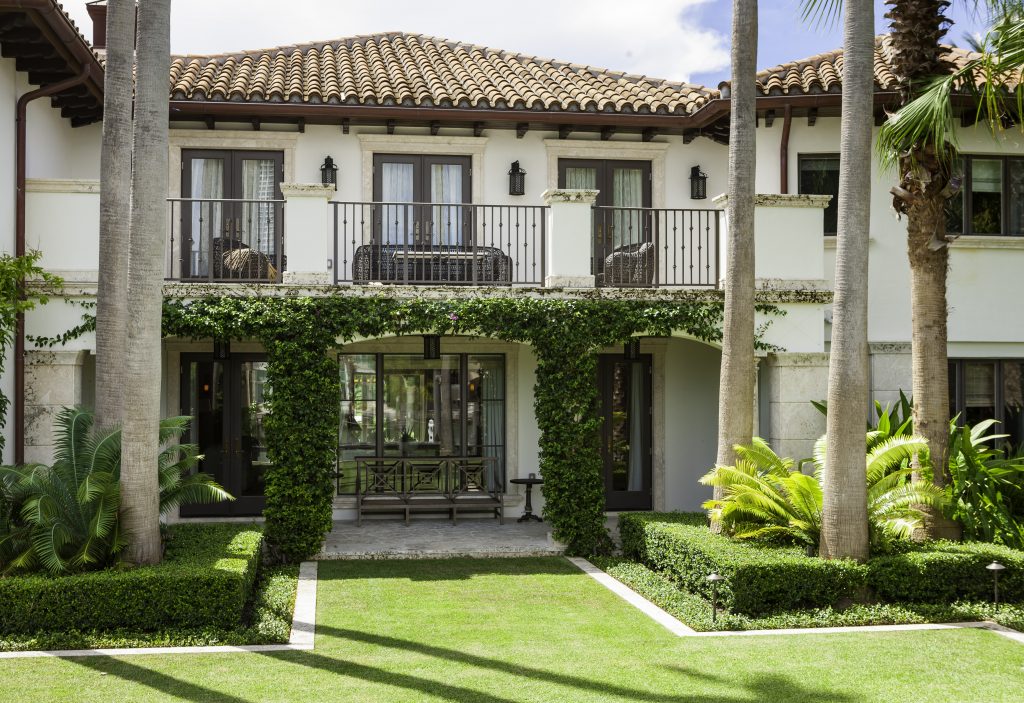 A two-story house with a tiled roof, palm trees, and well-maintained greenery. White facade with balconies and large windows.