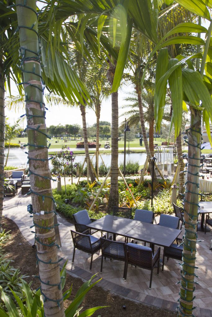 A tranquil garden setting with palm trees, outdoor seating, and a view of a landscaped golf course and water feature in the background.